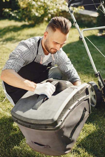 A man with neatly styled hair and a short beard is dressed in a checkered shirt and wearing gardening gloves while performing garden maintenance outdoors. He is inspecting or adjusting a large black a